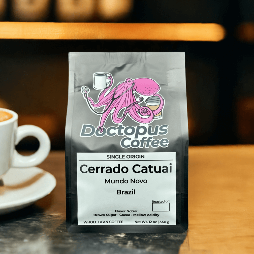 Doctopus Coffee's Cerrado Catuai Brazilian coffee bag displayed in cafe setting with white coffee cup visible. Label shows brown sugar and cocoa flavor notes