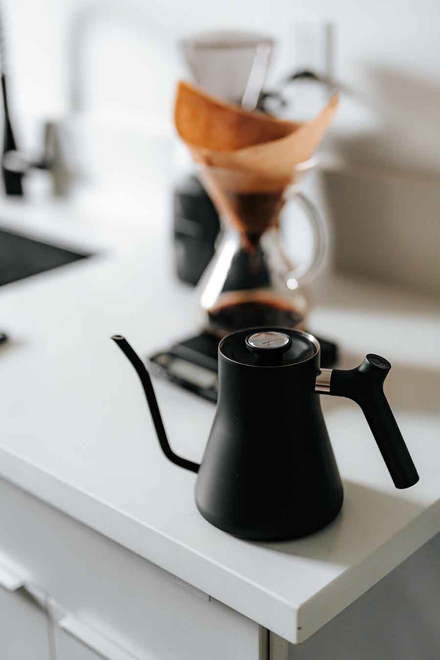 Pour-over coffee brewing setup with black gooseneck kettle and Chemex brewer